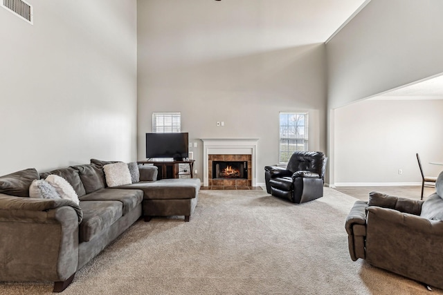 living area with carpet, visible vents, a towering ceiling, a tile fireplace, and baseboards