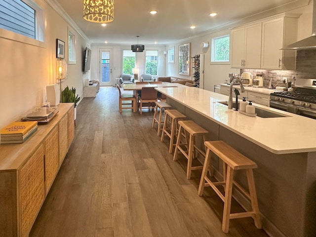 kitchen with white cabinetry, open floor plan, wall chimney exhaust hood, an island with sink, and a kitchen bar