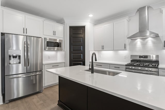 kitchen with light countertops, appliances with stainless steel finishes, white cabinets, a sink, and wall chimney exhaust hood