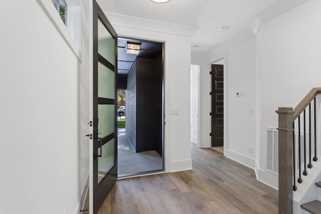 hall featuring wood finished floors, visible vents, baseboards, stairway, and crown molding