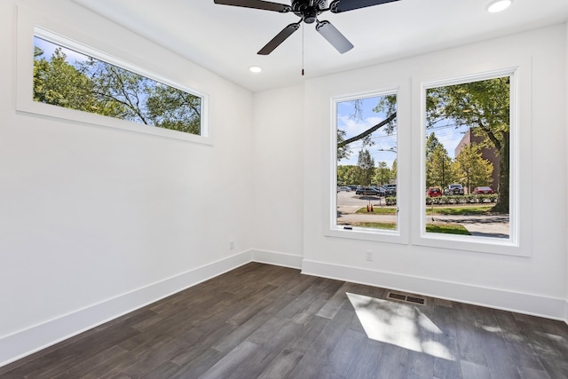 empty room with a wealth of natural light, dark wood-style flooring, visible vents, and baseboards