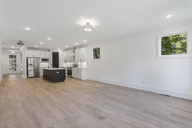 kitchen featuring a kitchen island with sink, stainless steel appliances, open floor plan, light countertops, and wall chimney exhaust hood