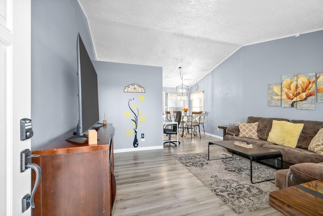 living room featuring baseboards, vaulted ceiling, wood finished floors, and a chandelier