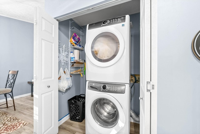 laundry room featuring light wood finished floors, baseboards, laundry area, and stacked washer / dryer