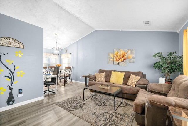 living room featuring lofted ceiling, a notable chandelier, wood finished floors, visible vents, and baseboards