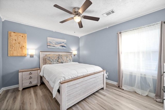 bedroom featuring baseboards, crown molding, visible vents, and light wood-style floors