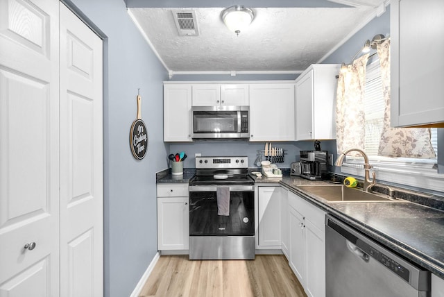 kitchen with dark countertops, appliances with stainless steel finishes, light wood-type flooring, white cabinetry, and a sink