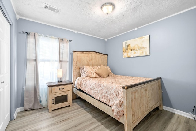 bedroom featuring a textured ceiling, light wood-type flooring, visible vents, and baseboards