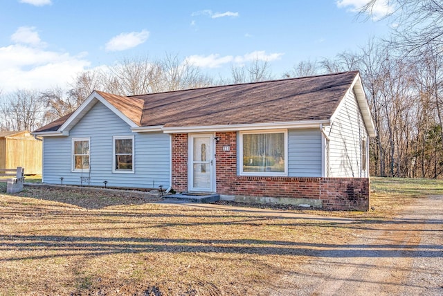 ranch-style home featuring roof with shingles, a front yard, and brick siding