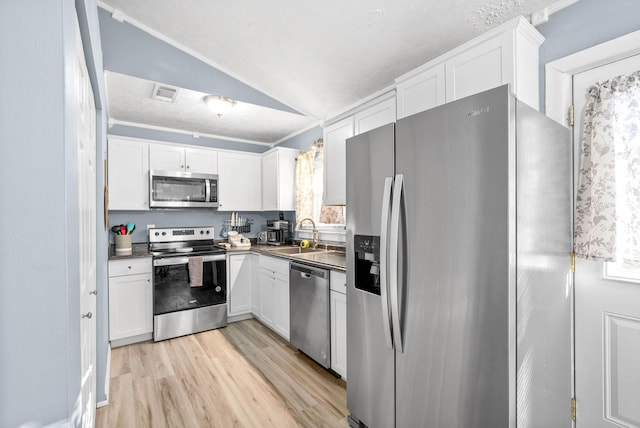 kitchen with dark countertops, lofted ceiling, appliances with stainless steel finishes, white cabinets, and a sink