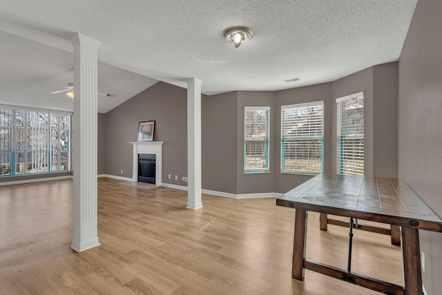 interior space featuring light wood-style floors, a fireplace with flush hearth, a ceiling fan, and ornate columns