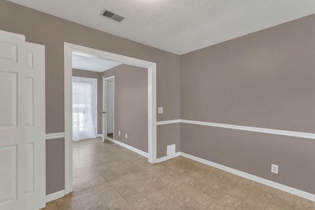 empty room featuring visible vents, a textured ceiling, and baseboards