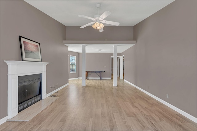 unfurnished living room with light wood-style floors, baseboards, a ceiling fan, and a glass covered fireplace