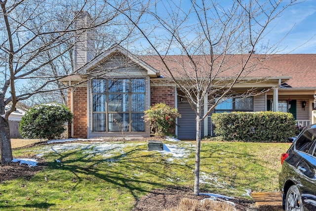 single story home with brick siding, roof with shingles, a chimney, and a front yard