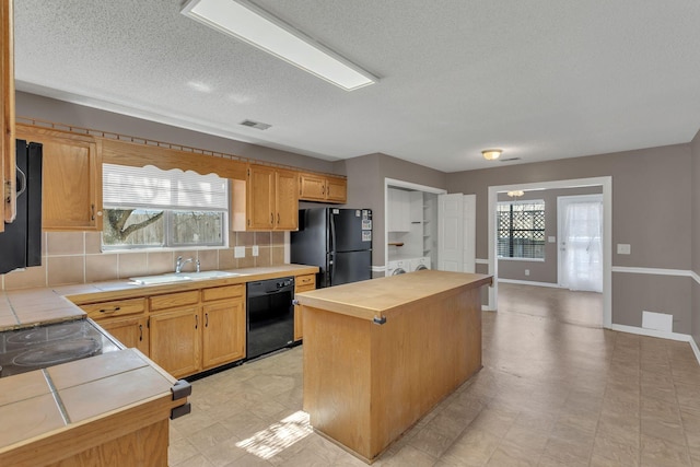 kitchen with light floors, tile counters, decorative backsplash, a kitchen island, and black appliances