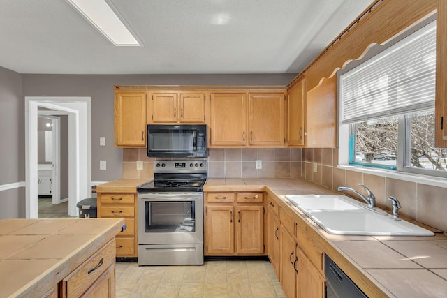 kitchen featuring tile countertops, black appliances, a sink, and decorative backsplash