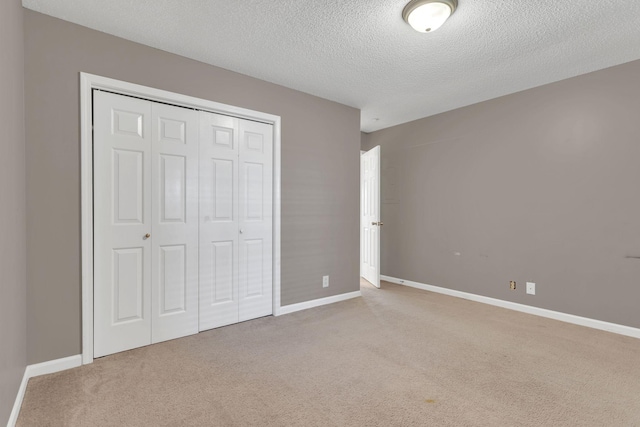 unfurnished bedroom with a textured ceiling, carpet floors, a closet, and baseboards