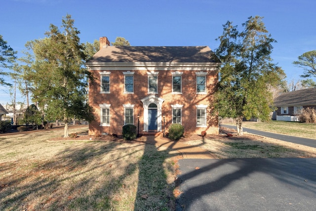 colonial house featuring brick siding, a chimney, and a front lawn