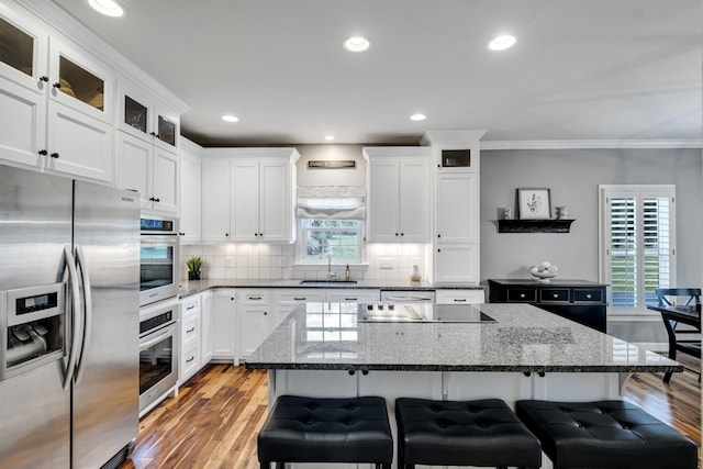 kitchen featuring a sink, a kitchen island, stainless steel fridge with ice dispenser, dark stone counters, and a kitchen bar