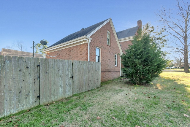 view of home's exterior featuring brick siding, a yard, and fence