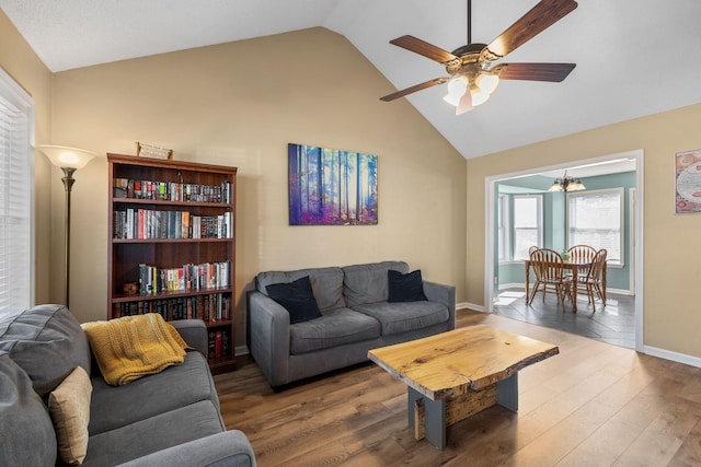 living room with high vaulted ceiling, ceiling fan with notable chandelier, baseboards, and wood finished floors