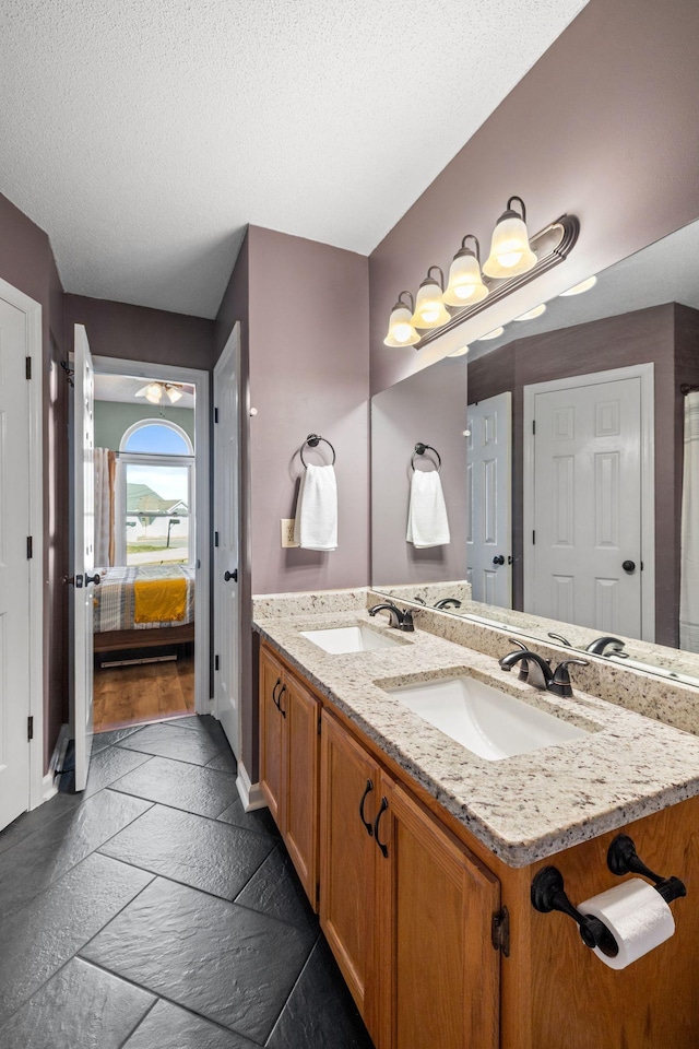 full bath featuring a textured ceiling, double vanity, a sink, and stone tile flooring