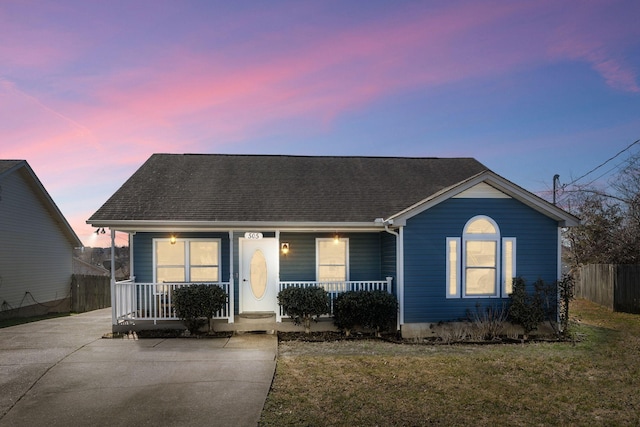 view of front facade with covered porch, a shingled roof, fence, and a front yard