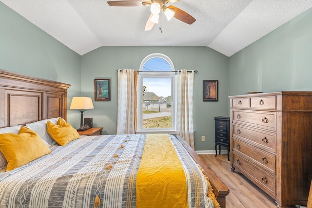 bedroom featuring baseboards, a ceiling fan, vaulted ceiling, a textured ceiling, and light wood-type flooring