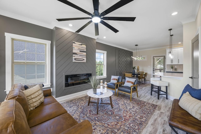 living room with baseboards, light wood-style flooring, crown molding, a fireplace, and recessed lighting