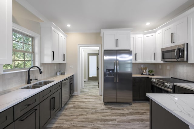 kitchen with light stone counters, white cabinetry, stainless steel appliances, and a sink