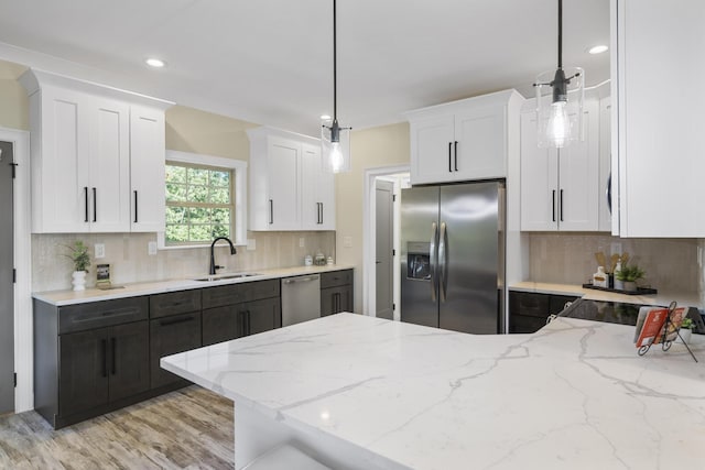 kitchen with appliances with stainless steel finishes, pendant lighting, white cabinets, and a sink