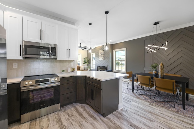 kitchen featuring light wood-style flooring, stainless steel appliances, white cabinets, light countertops, and pendant lighting