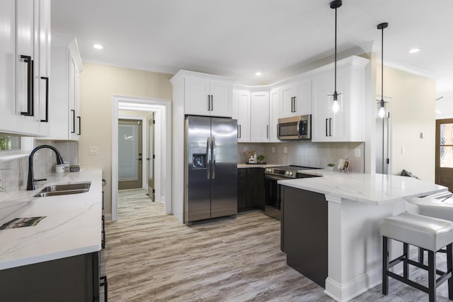 kitchen with appliances with stainless steel finishes, decorative light fixtures, a peninsula, white cabinetry, and a sink