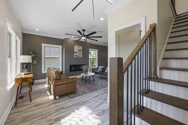 living room with stairway, ornamental molding, a large fireplace, light wood-type flooring, and baseboards