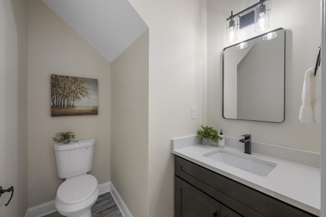 half bathroom featuring baseboards, toilet, wood finished floors, vaulted ceiling, and vanity