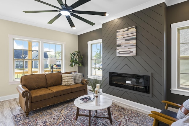 living area featuring ceiling fan, a large fireplace, wood finished floors, baseboards, and ornamental molding