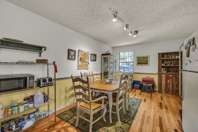 dining space with light wood-style flooring, track lighting, and a textured ceiling