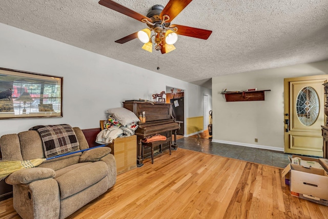 living room with a ceiling fan, a textured ceiling, baseboards, and wood finished floors