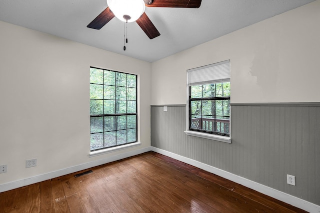 unfurnished room with wood-type flooring, a healthy amount of sunlight, visible vents, and wainscoting