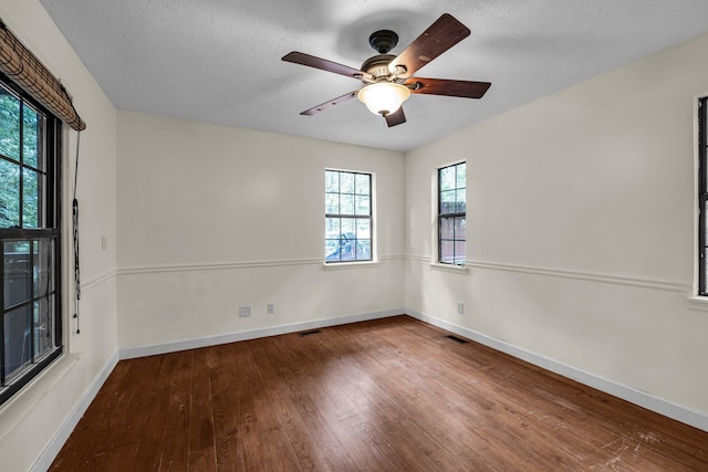 empty room with a textured ceiling, hardwood / wood-style flooring, visible vents, and baseboards