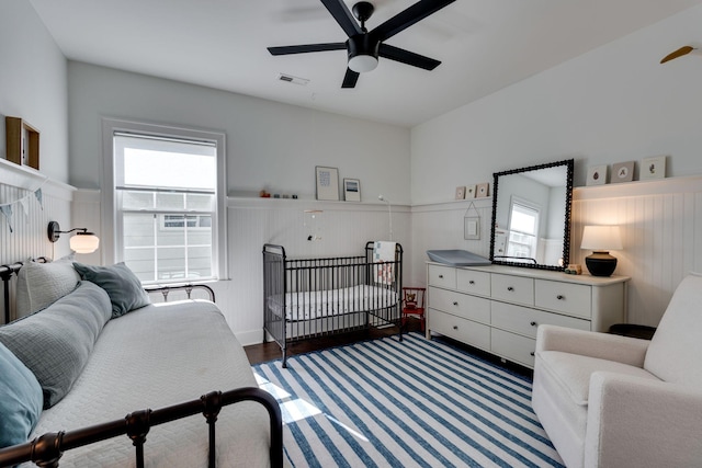 bedroom featuring a wainscoted wall, ceiling fan, multiple windows, and visible vents