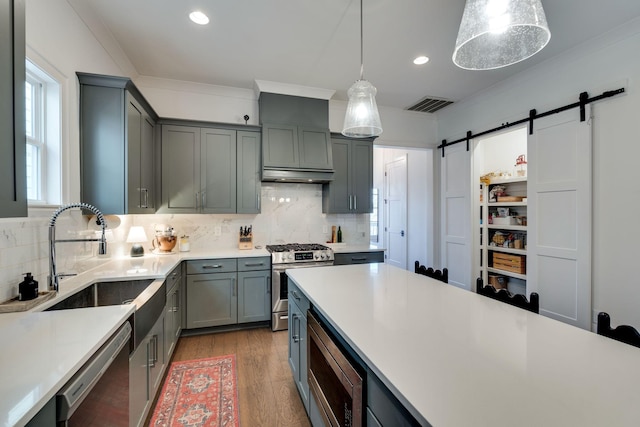 kitchen with light countertops, hanging light fixtures, visible vents, a barn door, and appliances with stainless steel finishes