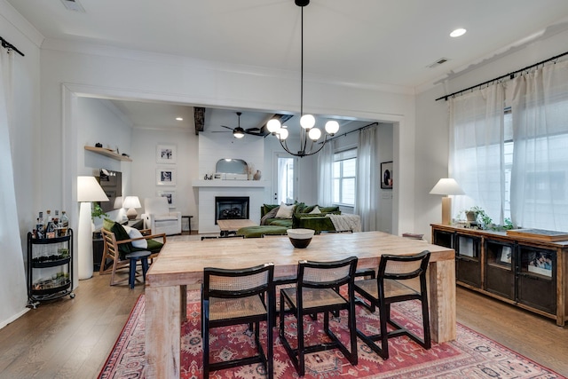 dining area featuring a large fireplace, ornamental molding, wood finished floors, and visible vents