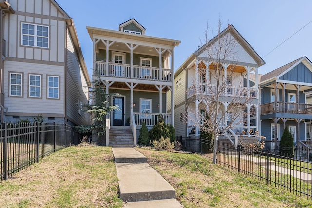 view of front of home featuring a balcony, covered porch, a fenced front yard, and a front lawn