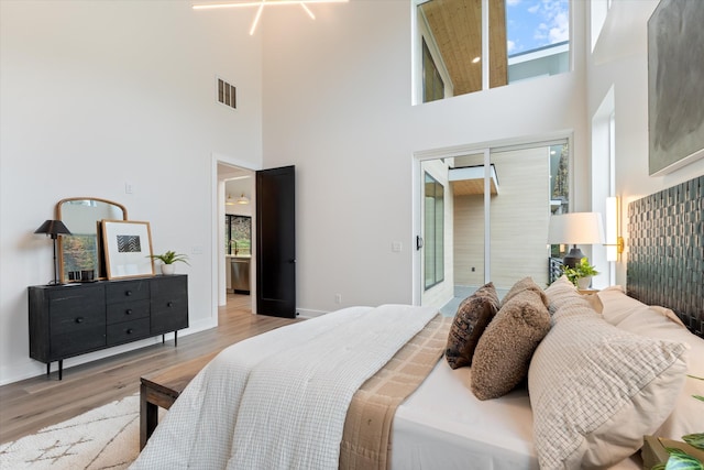 bedroom featuring a towering ceiling, visible vents, baseboards, a closet, and light wood finished floors