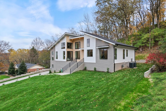 contemporary home with central AC unit, a front lawn, and brick siding