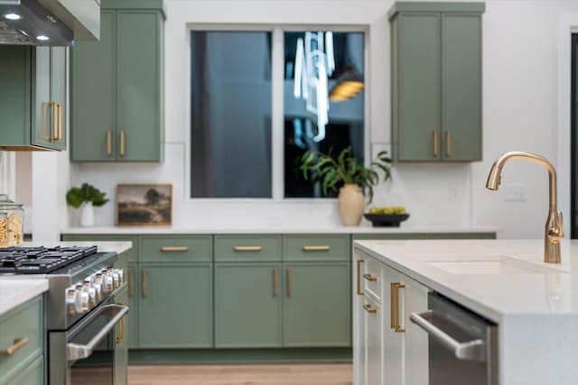 kitchen featuring stainless steel appliances, light countertops, a sink, green cabinetry, and exhaust hood