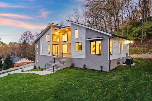 contemporary house featuring brick siding, a lawn, and stairs