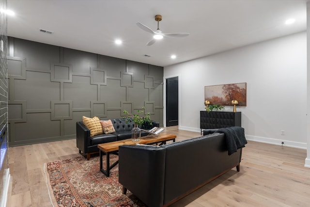 living area featuring visible vents, a decorative wall, light wood-style floors, ceiling fan, and baseboards