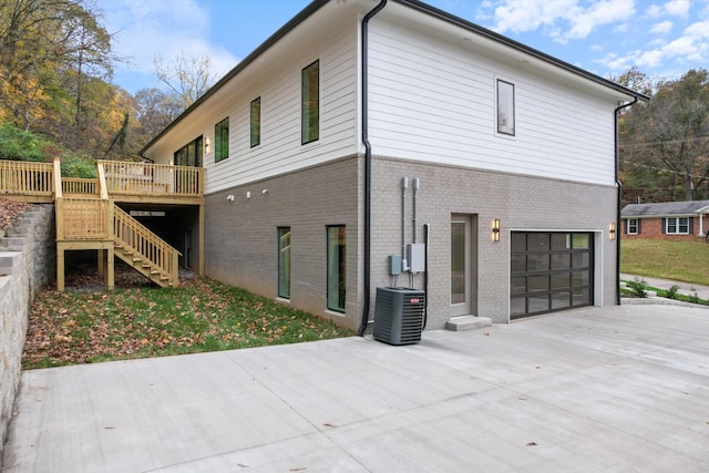 view of home's exterior featuring driveway, central AC unit, stairs, a deck, and brick siding